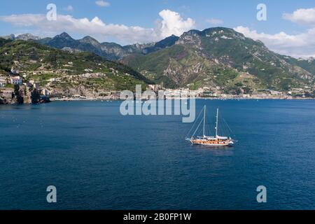 Eine Yacht vor der Amalfiküste an einem hellen Sommertag in Italien, mit der Berglandschaft dahinter. Stockfoto