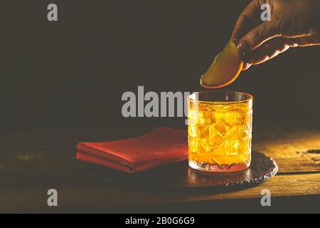 Frau Hand schmückt orangefarbenen alkoholisierten Cocktail negroni des Glases. Trinken Sie mit Gin, Campari Martini Rosso und Orange, einem italienischen Cocktail, einem ap Stockfoto