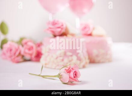 Zwei Minikuchen, eine Brille mit rosafarbenem Traubenwein und Rosenblumen auf einem weißen Tisch. Romantisches Dinner Konzept. Stockfoto