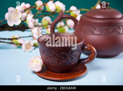Braune Keramikteapot und Tasse mit Tee. Auf dem Hintergrund blüht Kirschzweig Sakura. Asiatischer orientalischer Stil. Federkonzept. Stockfoto