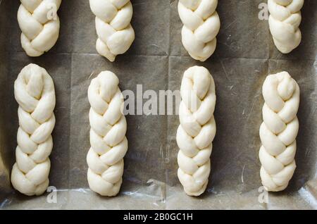 Vorbereitung - raw ungebackene Gebäck. Hefeteig Brötchen auf Backpapier, close-up. Im rustikalen Stil. Traditionelles Gebäck Stockfoto