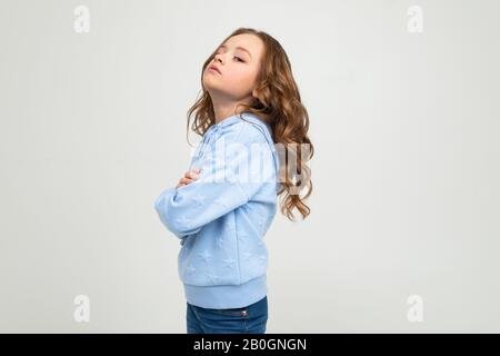 Beleidigtes Teenager-Mädchen in einem blauen Hoodie überquerte ihre Arme und hob ihr Kinn auf einem weißen Hintergrund auf Stockfoto