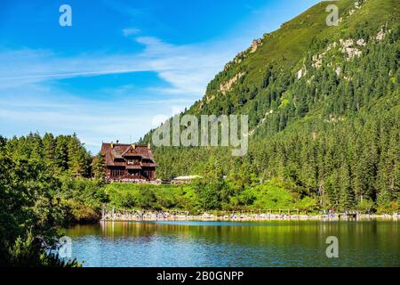 Panoramablick auf den Morskie Oko Bergsee rund um Lärche, Kiefer und Fichte mit Schronisko Przy Morskim Oku Schutzhaus im Hintergrund Stockfoto