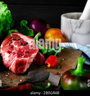 Zwei saftige Steaks liegen auf einem wilden Stein neben roten und grünen Chilischoten und einen frischen grünen Salat auf einem schwarzen Holztisch Stockfoto