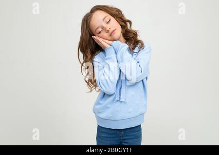 Schlafendes Teenager-Mädchen in zwanglosem blauen Hoodie schläft auf hellgrauem Studiohintergrund ein Stockfoto