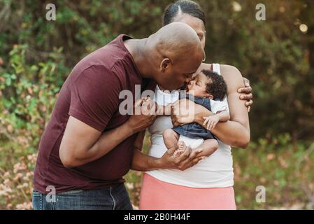 Schließen Sie glückliche Mutter und Vater, die neugeborenes Mädchen küssen Stockfoto