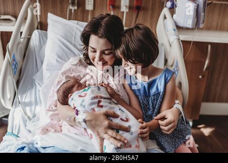 Mittelansicht der Mutter, die einen neugeborenen Sohn hält, der Geschwister trifft Stockfoto