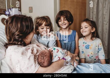 Seitenansicht der Mutter, die einen neugeborenen Sohn hält, der Geschwister trifft Stockfoto