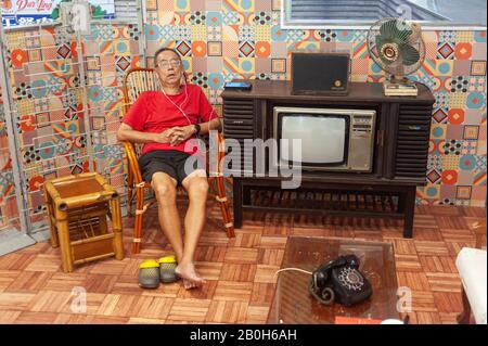 17.01.2020, Singapur, Singapur - Im Einkaufszentrum Cross Street Exchange sitzt ein älterer Mann auf einem Stuhl in einer Nachbildung eines typischen Wohnzimmerwitts Stockfoto