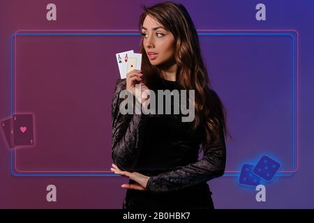 Frau in schwarzem Samtkleid. Zwei Asse zeigen, auf farbenfrohem Hintergrund posieren. Collage mit Neon-Rahmen, Würfel, Spielkarten. Poker, Casino. Nahaufnahme Stockfoto