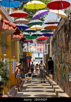 Streetart und Sonnenschirme sorgen für Farbe und Schatten auf Callejon Angosto in Gettemani, Cartagena, Kolumbien Stockfoto