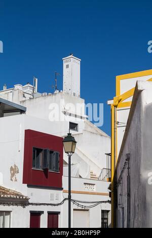 Überwiegend weiße Fassaden der Häuser mit bunten Details weißer Kamin und einer Straßenlaterne - Laterne. Strahlend blauer Himmel. Alvor, Algarve, Portugal. Stockfoto