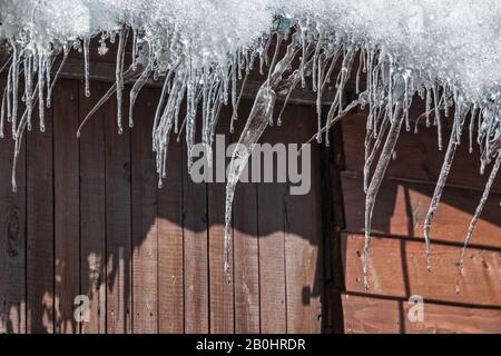 Eiszapfen hängen am frühen Morgen am Dach eines Hauses an einem sonnigen Frühlingstag. Stockfoto