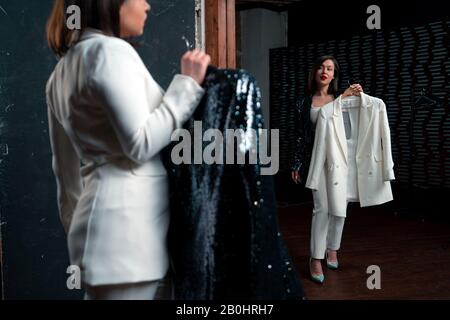 Attraktive Schöne Frau, Die Kostüm Für Leistung Wählt Und Ihr Spiegelbild Im Big Mirror betrachtet. Outfit Im Spiegel Ist Schwarz Und Weiß In Real Stockfoto