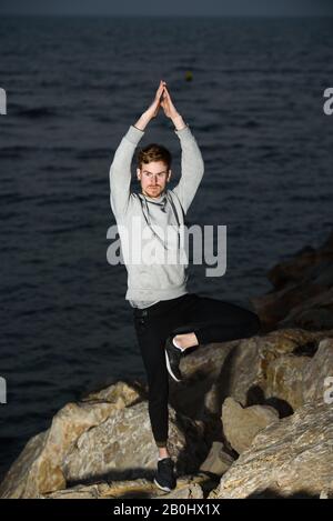 Junger Mann in Namaste-Grußposition, während er seinen Geist von Sorgen in Baumpose befreit. Stockfoto