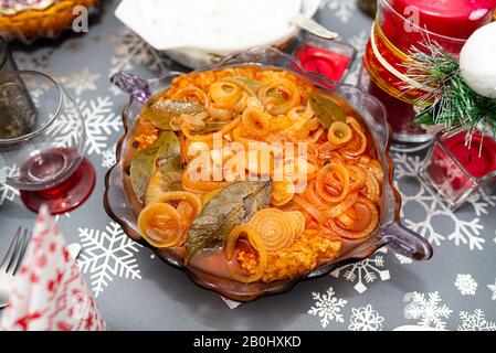 Fischfilets in Brotkrümeln in Öl und Zwiebeln, in einer Schüssel auf dem Weihnachtstisch in Polen stehend. Stockfoto