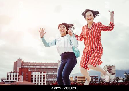 Asiatische Mutter und Tochter springen draußen - Fröhliche Familie hat Spaß beim Tanzen und Feiern im Freien - Konzept der Senioren und Jugendlichen Stockfoto