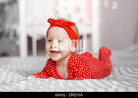 Ein kleines neugeborenes Mädchen liegt auf ihrem Bauch und lacht. Rote Kleidung und Kopfschmuck. Das Konzept der Mutterschaft, der Kinderbetreuung und der Familie. Stockfoto