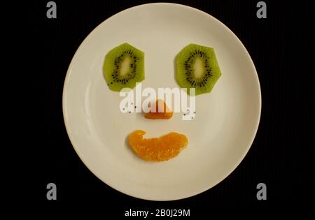 Smiley-Gesicht aus Kiwi-, Papaya- und Orangenscheiben. Stockfoto