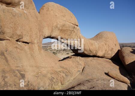 Steinformation aus Felsbogen aus Sandstein von Spitzkoppe Erongo in Namibia mit Blick auf Berge im Hintergrund Stockfoto