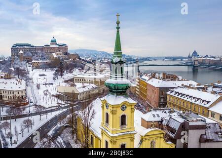 Budapest, Ungarn - katholische Kirche mit schneebedecktem Buda-Viertel, Königspalast der Burg Buda, Varkert Basar, Szechenyi-Kettenbrücke und Parlament am Rücken Stockfoto