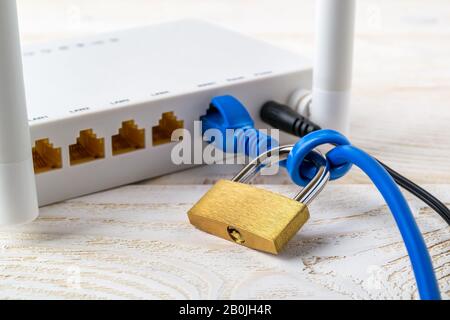 Weißer WLAN-Router mit Vorhängeschloss auf einem Netzwerkkabel auf einem weißen Holztisch. Verbotene oder eingeschränkte Konzepte der Internet- und Internetzensur. Stockfoto