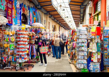 Larnaca, ZYPERN - 16. FEBRUAR 2020: Souvenirmarkt für Touristen im Pavillon, Menschen, die in Reihe zwischen Geschäften mit Waren laufen Stockfoto