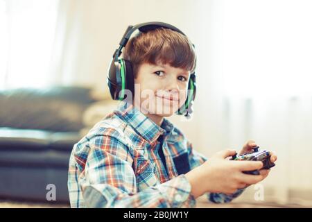 Kleiner Gamer Junge im Headset, der Controller hält und in die Kamera lächelt Stockfoto