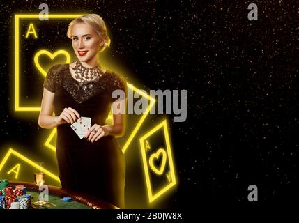 Dame in schwarzem Kleid mit Assen, lächelnd, posiert am Tisch mit Pommes und Champagner darauf. Schwarzer Hintergrund mit Neon-Spielkarten. Poker, Casino Stockfoto