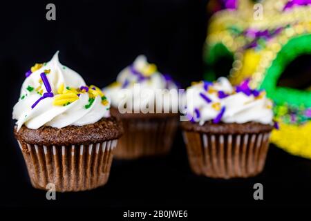 Drei kleine Cupcakes auf schwarzem Hintergrund mit einer Maske, die im Hintergrund verschwommen ist. Geringe Schärfentiefe. Stockfoto