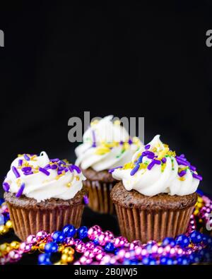 Drei kleine Cupcakes auf schwarzem Hintergrund mit bunten Perlen. Kopiere den Bereich oben. Stockfoto