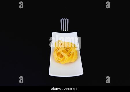 Edelstahlgabel und Tagliatelle Pasta auf dem weißen Teller. Diät-Mittagessen. Stockfoto