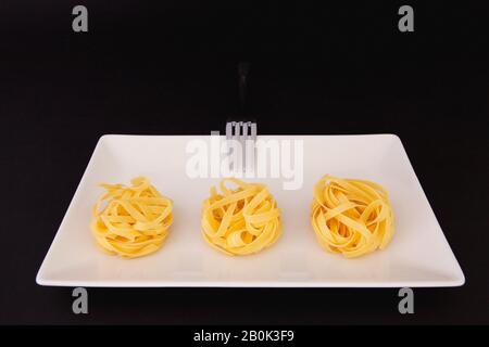 Edelstahlgabel und Tagliatelle Pasta auf dem weißen Teller. Diät-Mittagessen. Stockfoto