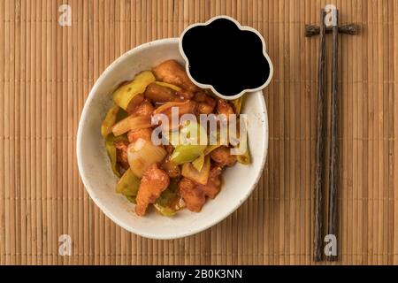 Schüssel mit süßem und saurem Huhn und leerem Kelch auf einem Tisch Stockfoto