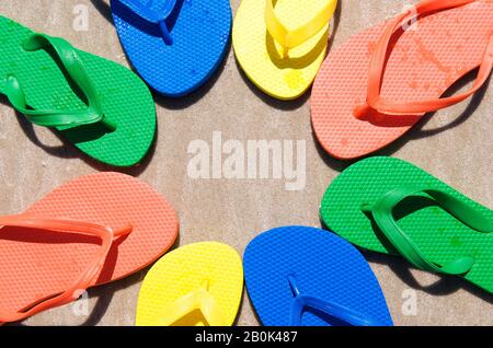 Kreis von Flip-Flops in hellen Sommerfarben am glatten Sandstrand Stockfoto