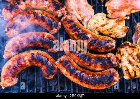 Schweinefleisch und Würstchen auf einem Holzkohlegrill gegrillt. Draufsicht auf leckeres Barbecue, Essenskonzept, Grillspezialitäten und Details zu Grillgerichten Stockfoto