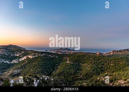 Sonnenaufgang in Calanque de Morgiou (Marseille, Frankreich): Der atemberaubende Blick auf die Bergwelt der Klippen und die Insel Riou in der Ferne unter Th Stockfoto