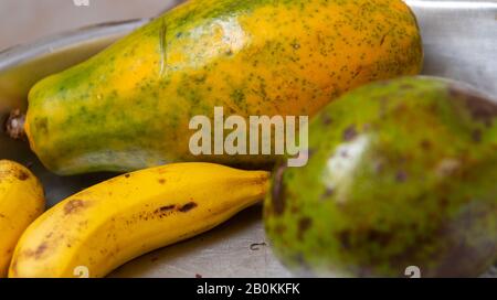 Ein Tablett mit tropischen und traditionellen brasilianischen Früchten, mit Papaya im Vordergrund, einem Avocado und zwei gelben Bananen. Tropische Früchte. Stockfoto