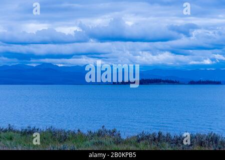 Blick über den blauen See auf die blauen Berge unter dem kalten bewölkten Himmel. Stockfoto