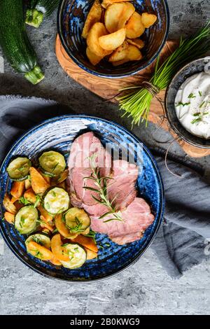 Geräucherter Schweinehals mit knusprigen gerösteten Kartoffeln und Zucchini-Scheiben auf einer Keramikplatte Stockfoto