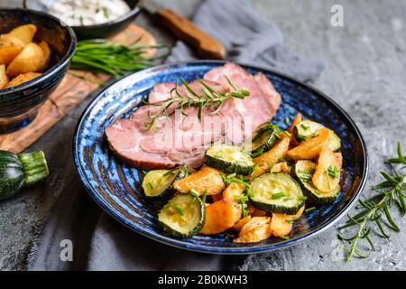 Geräucherter Schweinehals mit knusprigen gerösteten Kartoffeln und Zucchini-Scheiben auf einer Keramikplatte Stockfoto