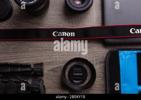 Fotoplatt lag auf einem grauen Holztisch. Schwarzer Canon-Gurt mit roten Streifen im Fokus. Canon Objektive, Canon Kameraausrüstung Stockfoto