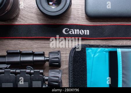Fotoplatt lag auf einem grauen Holztisch. Schwarzer Canon-Gurt mit roten Streifen im Fokus. Canon Objektive, Canon Kameraausrüstung Stockfoto