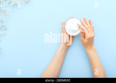 Handcreme, weibliche Hände, die organische Naturcremekosmetik auf einem pastellblauen Hintergrund auftragen. Hautpflegecreme im Mixbecher für Hände, Körper. Flaches Lay Stockfoto