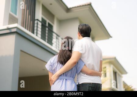 Hinteres Porträt des jungen asiatischen Paares, das zusammen steht und umarmt und vor ihrem neuen Haus glücklich aussieht, um neues Leben zu beginnen. Familie, Alter, Zuhause, echt Stockfoto