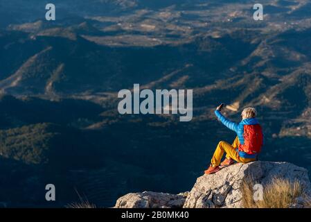 Junge Frau, die auf Felsen auf einem Berg steht und ein Selfie macht. Stockfoto