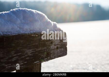 Holzfußbrücke mit Schnee und Sonnenschein während des Sonnenuntergangs auf dem zugefrorenen See Stockfoto