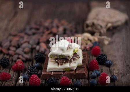 Weihnachtsschokolade. Schokoladenriegel mit Waldbeeren Obst und festlichem Hintergrund. Eine Auswahl an weißer, dunkler und Milchschokolade mit Stockfoto