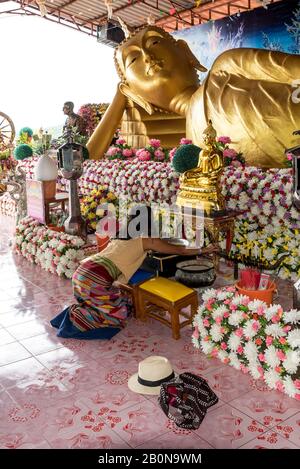 Frau, die im Wat betet, um Buddha zu verstellen, umgeben von Blumen in Pak Nam Pran, Thailand Stockfoto