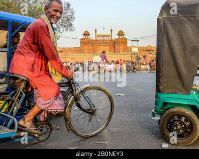 Ein älterer Mann, der auf einem Fahrradwagen inmitten des geschäftigen indischen Verkehrs reitet, lächelt, als er vorbeikommt, in der Nähe von Red Fort, Neu-Delhi 2018. Stockfoto